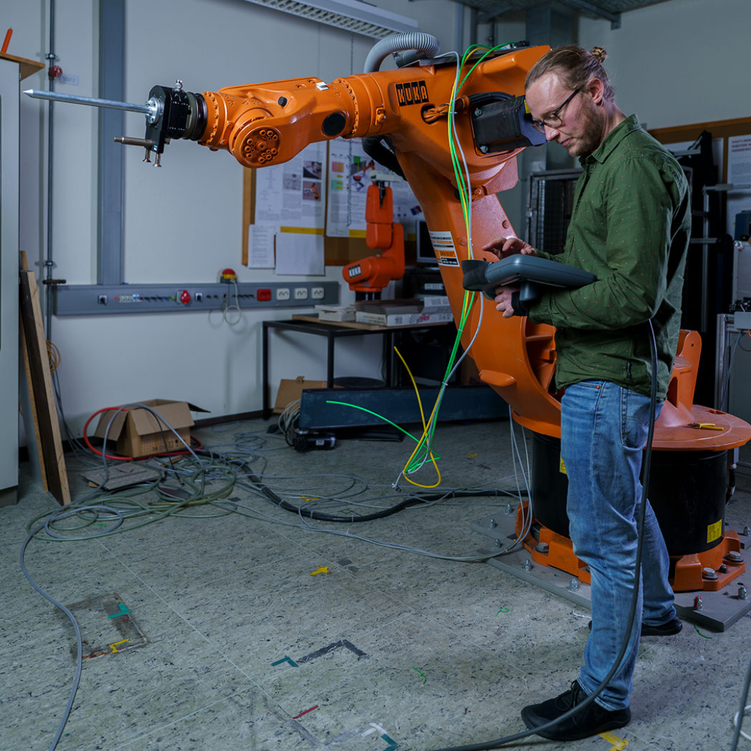 Bild mit einem Mann, der einen orangen Roboter von KUKA steuert
